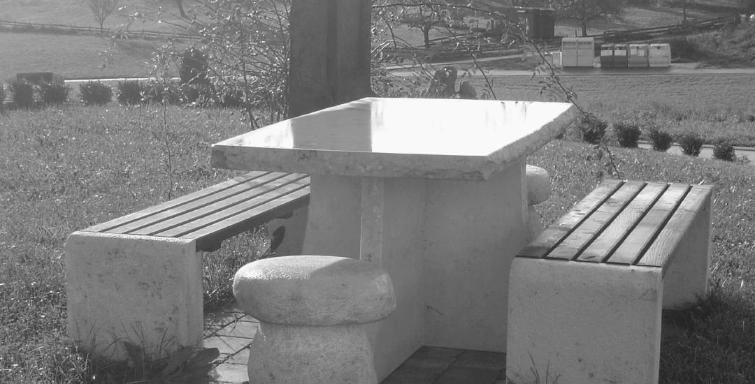 Es wird ein Tisch und zwei Bänke aus Stein abgebildet. Das Bild ist in schwarz weiß zu sehen.